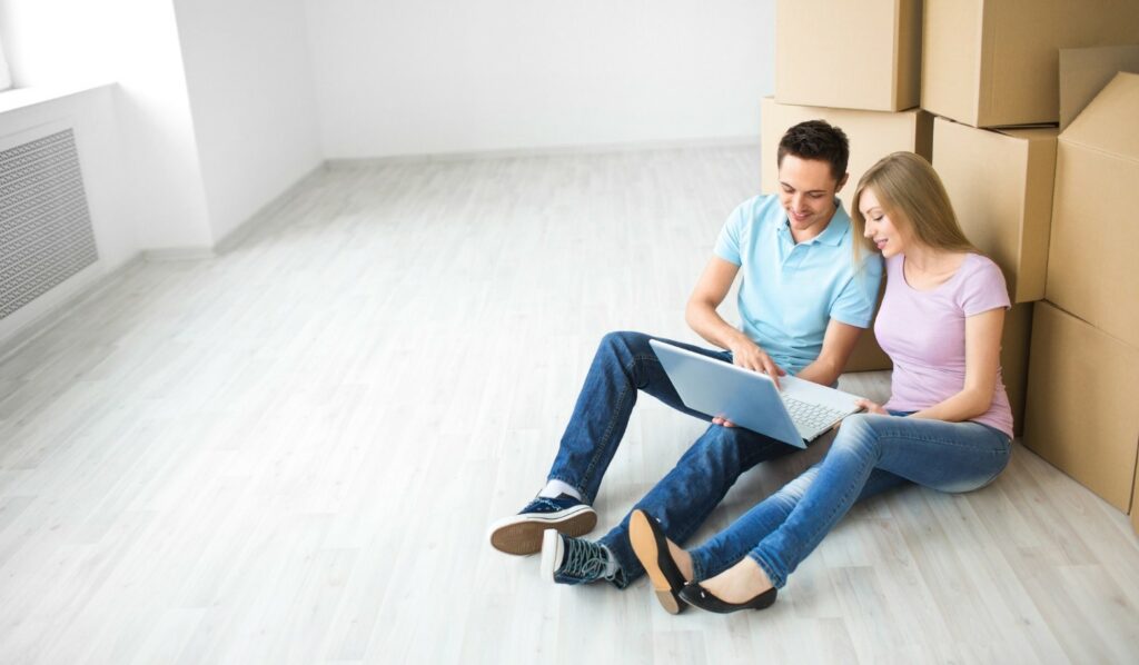 Couple looking at a laptop sitting in front of moving boxes.