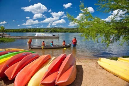 Family kayaking in a lake with kayaks lining the lake shore.
