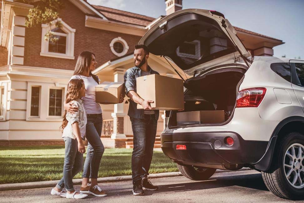 Family loading moving boxes into the trunk of a car.