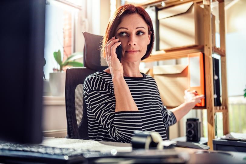 Business woman sitting in front of work computer while talking on the phone.