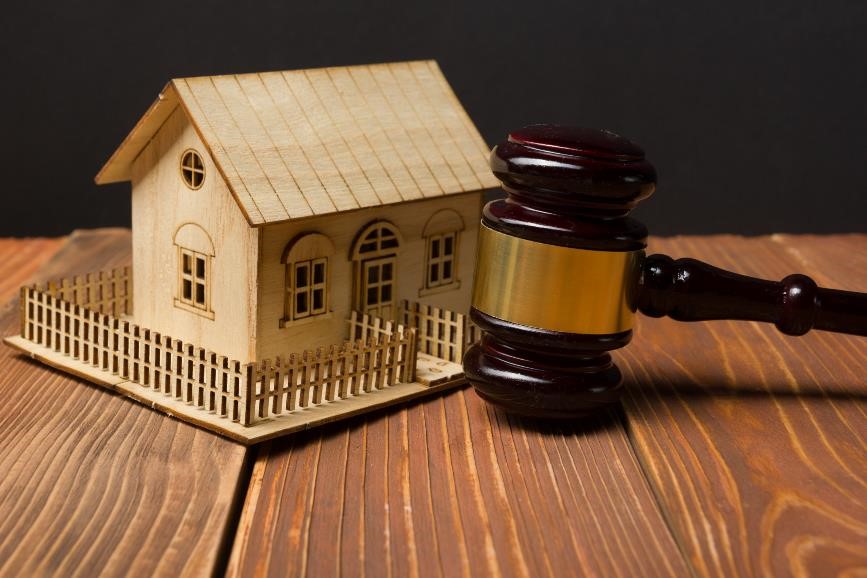 Miniature model of house sitting on table next to an auction gavel.
