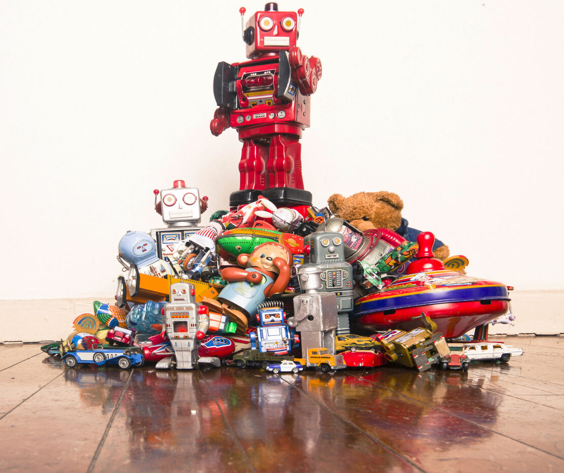 A red robot stands on top of a pile of collectible toys, such as a vintage teddy bear.