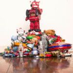 A red robot stands on top of a pile of collectible toys, such as a vintage teddy bear.