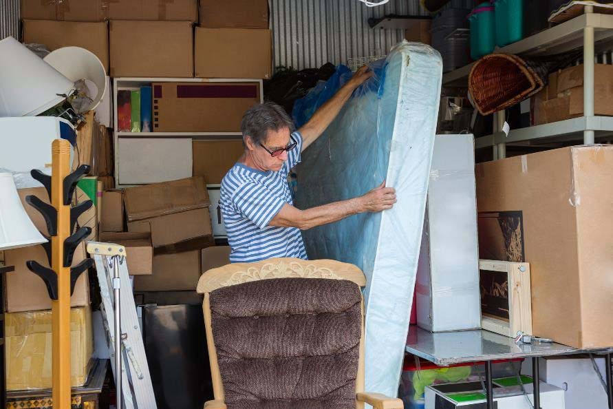 a man is reorganizing his storage unit that's packed with boxes, furniture, and a mattress