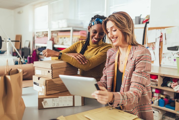 two female coworkers look at a tablet in their retail boutique