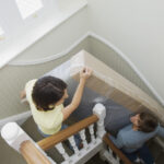 A woman and man carrying a mattress down the stairs.