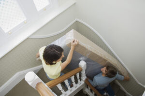 A woman and man carrying a mattress down the stairs.
