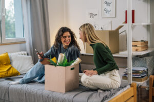 Two dorm roommates sitting on a bed next to a packed box.