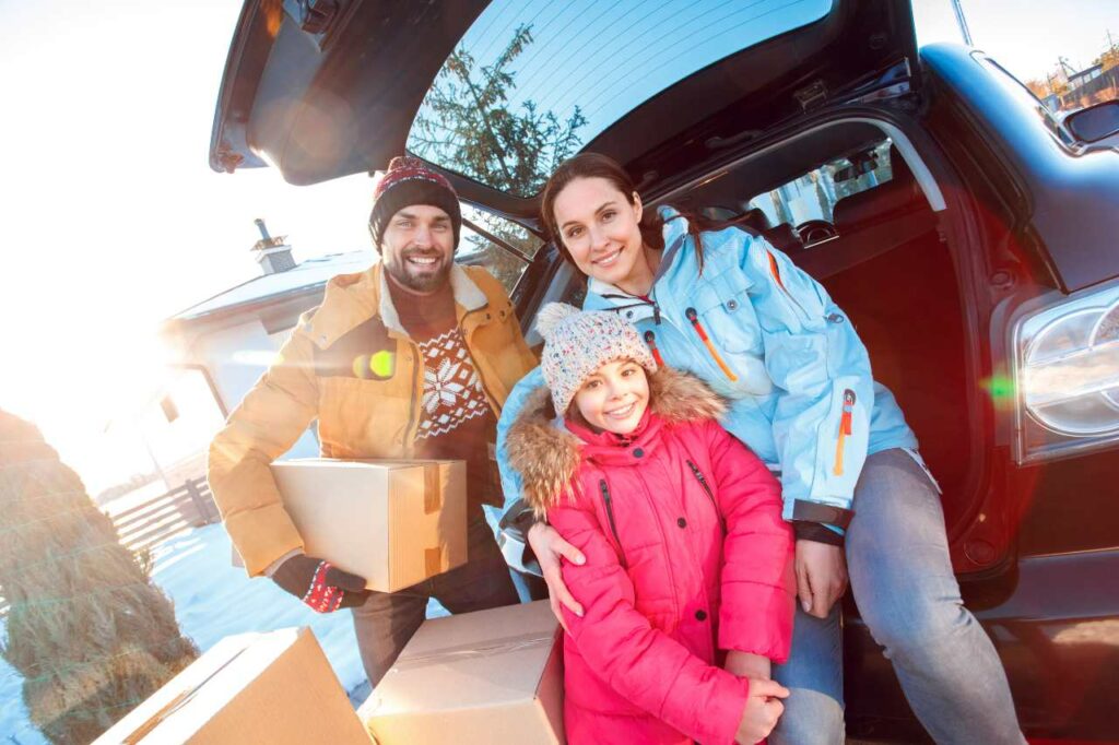 A young family sits in the back of their car with moving boxes