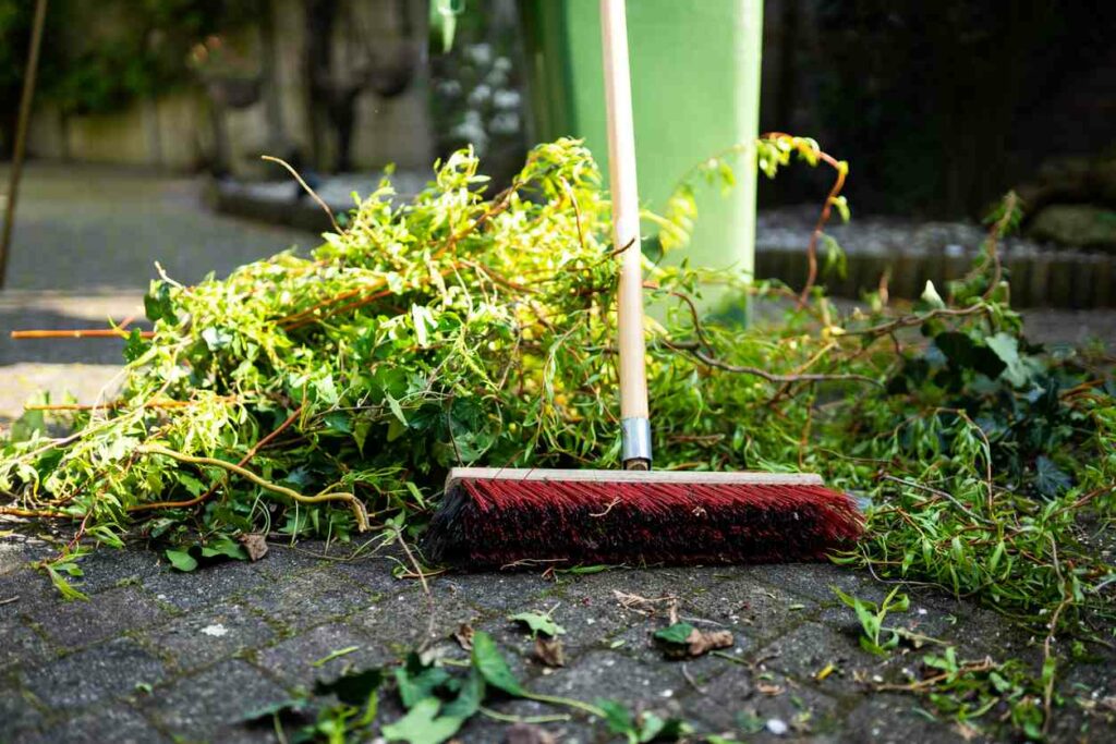 A broom sits next to a pile of weeds that have been pulled from a yard