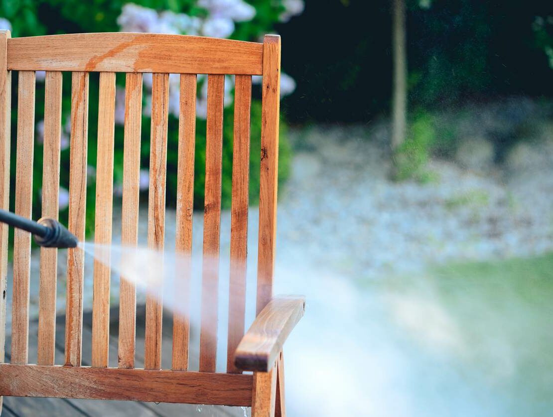 A wooden chair is cleaned in a backyard with a power washer