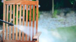 A wooden chair is cleaned in a backyard with a power washer