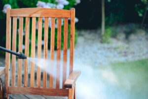 A wooden chair is cleaned in a backyard with a power washer