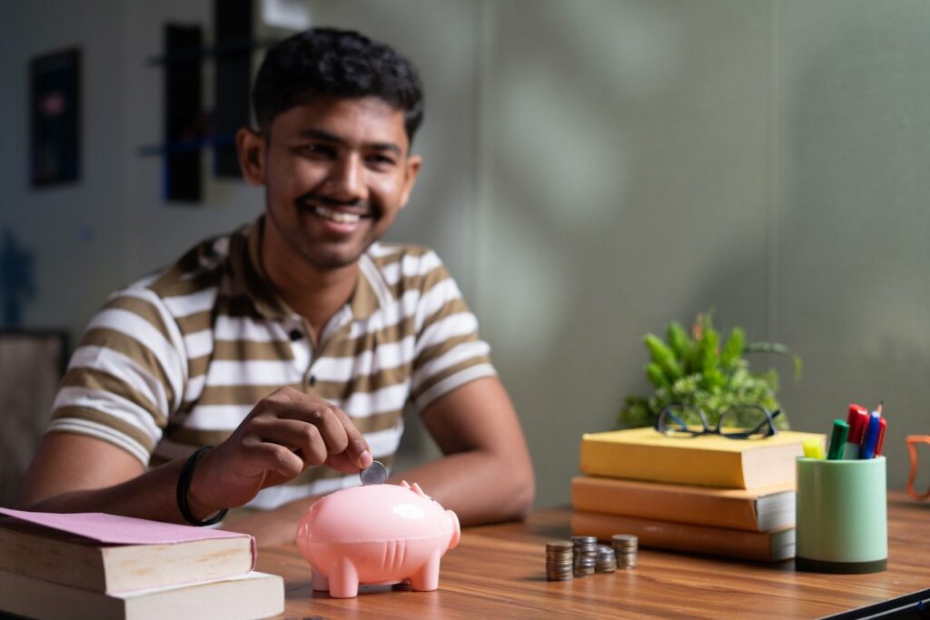 Young man puts quarters into a piggy bank on a wooden desk.