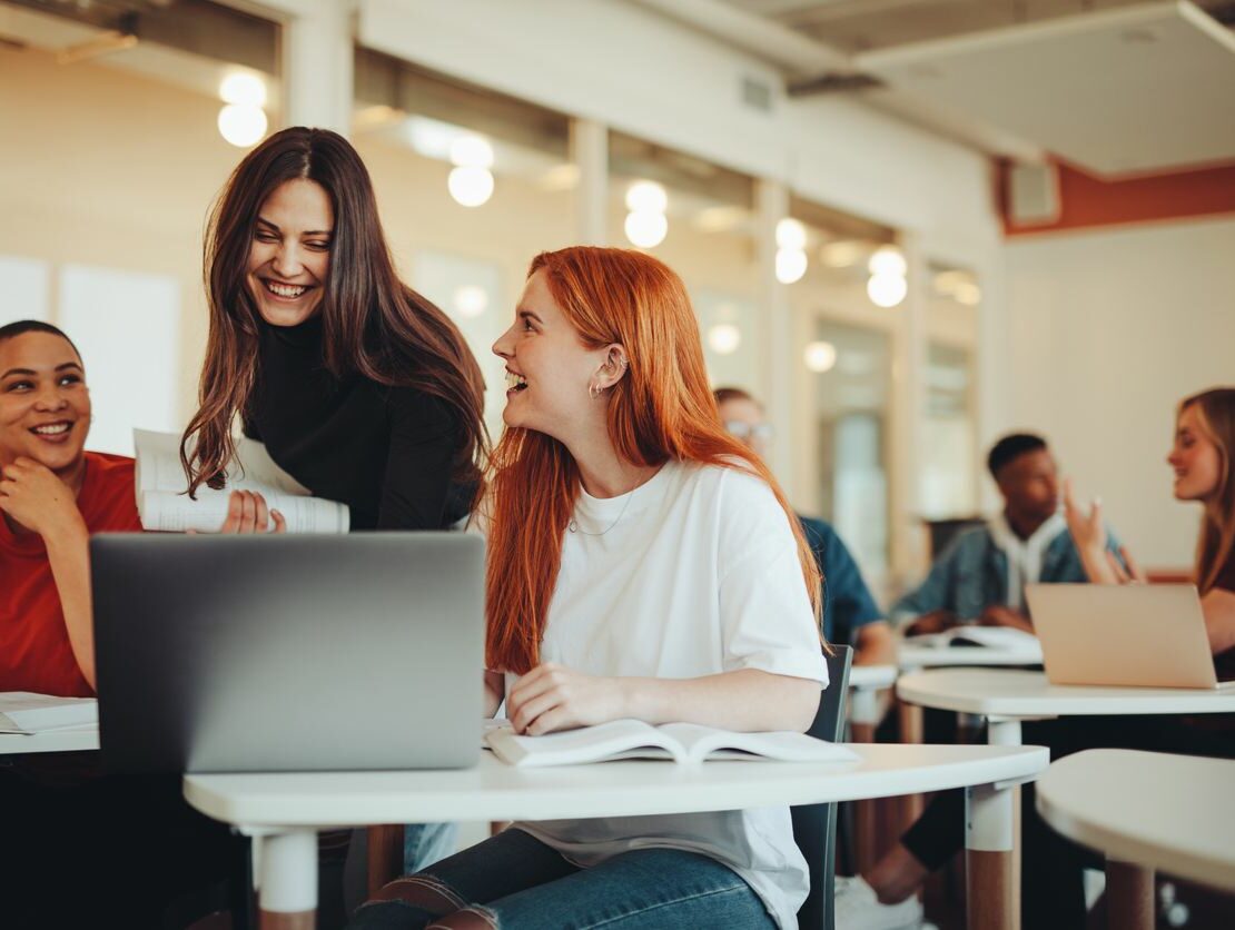 Three women gather around a laptop while looking and smiling at each other