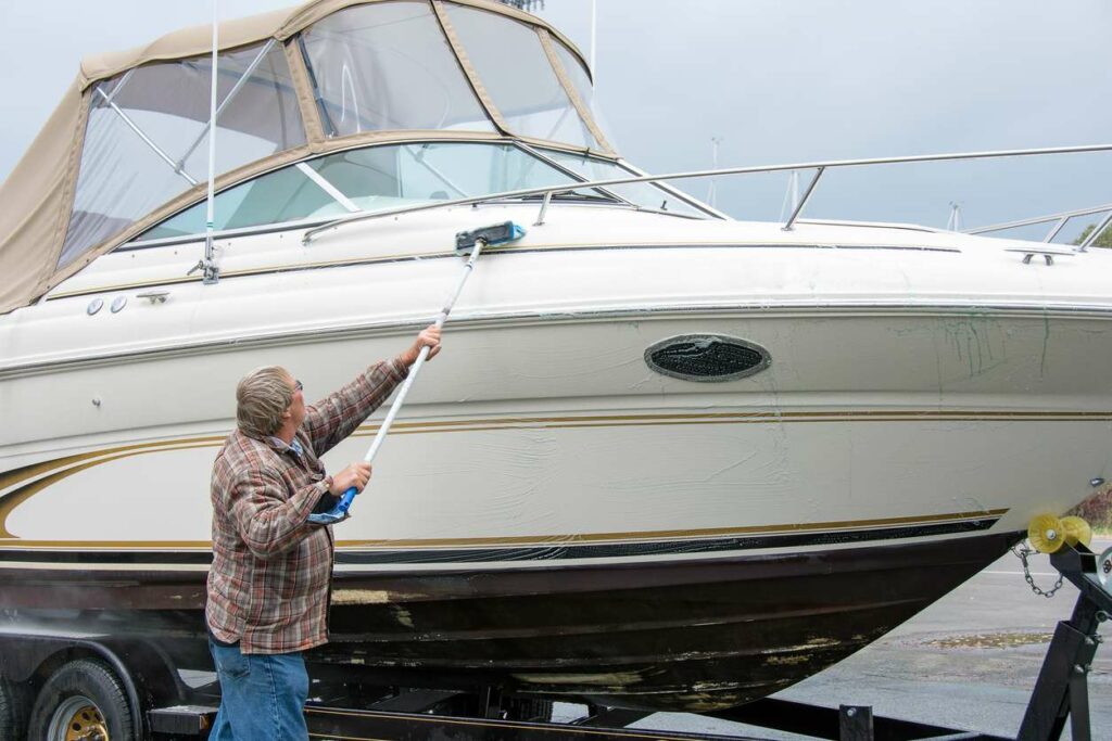 A man cleans a large boat using soapy water and an extended brush