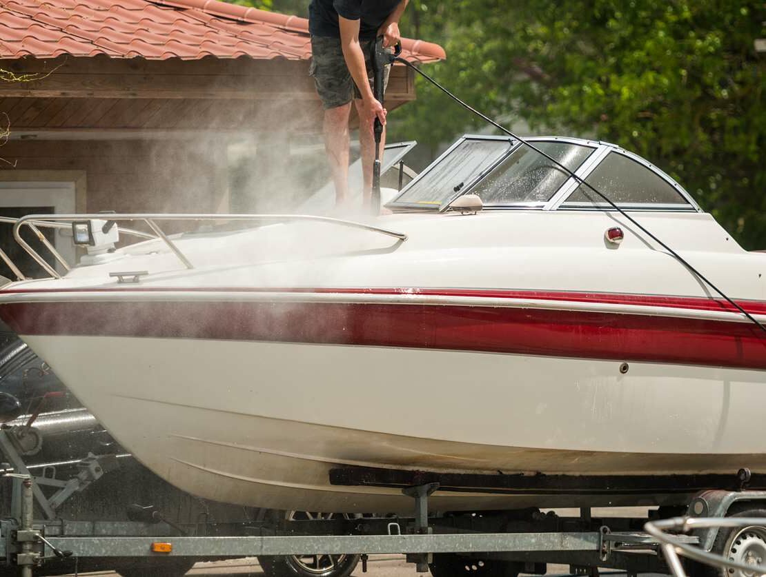 A boat on a trailer with a man power washing the boat to maintain its cleanliness
