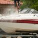 A boat on a trailer with a man power washing the boat to maintain its cleanliness