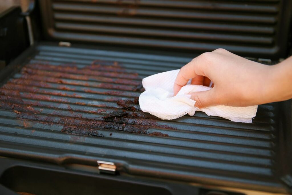 A person cleans a burnt grill with a white cloth