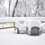 Patio furniture is covered in many inches of bright snow after a snowfall