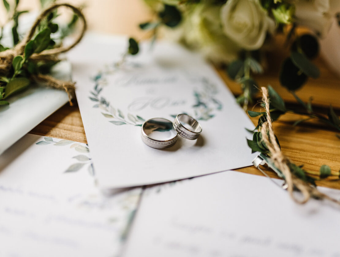 Stylish rings, flowers on wooden table background. Letters from the bride and groom.