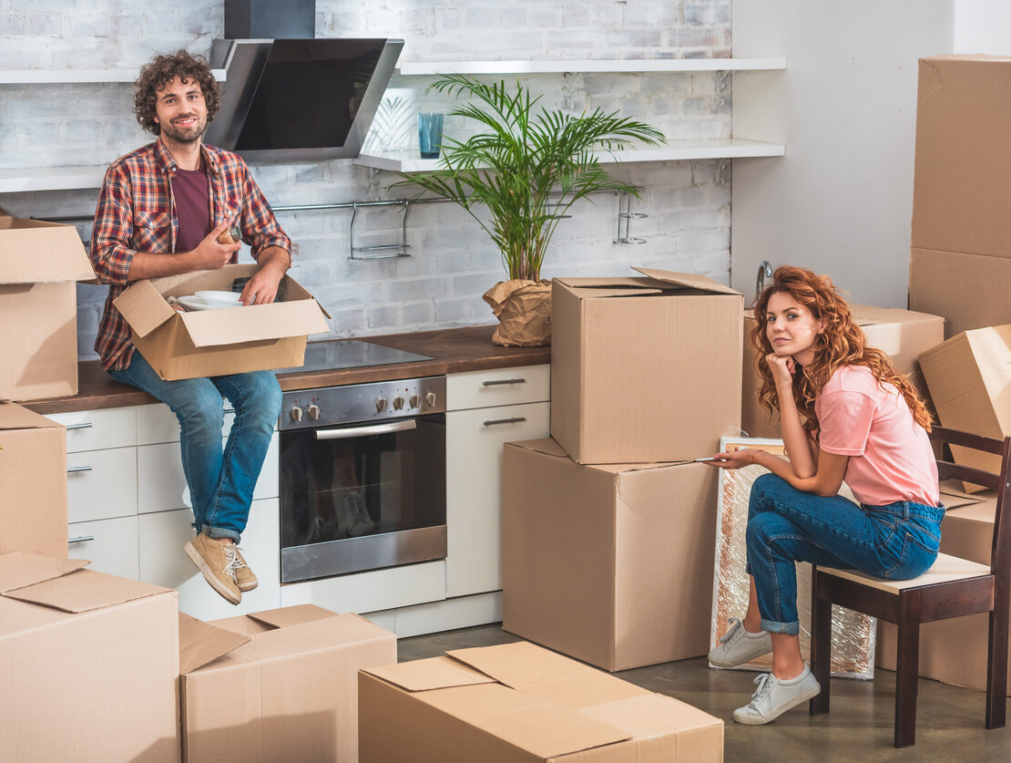 A man and woman unpacking boxes in their kitchen.