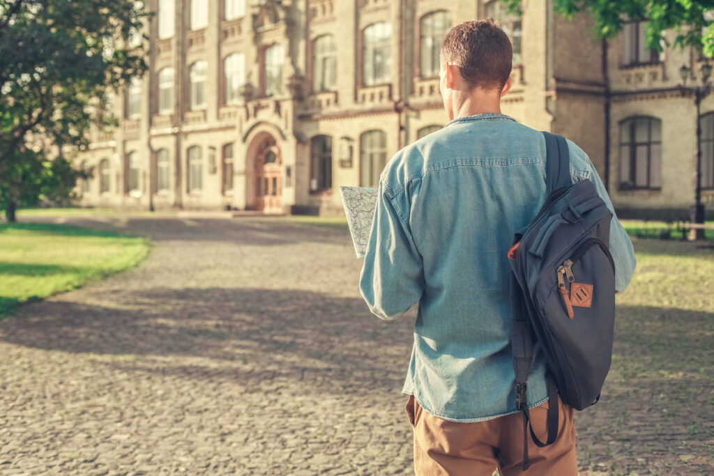 A college student looking at a map while walking around his college campus.