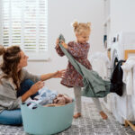 A mom and her young daughter taking laundry out of the hamper.