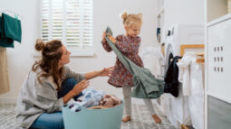 A mom and her young daughter taking laundry out of the hamper.