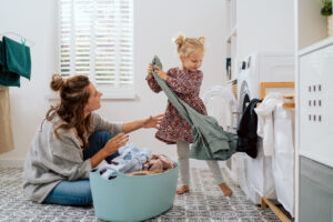 A mom and her young daughter taking laundry out of the hamper.