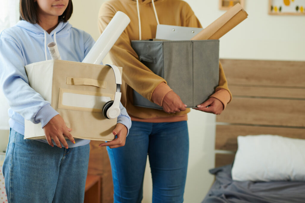 Two college students holding boxes in their freshman dorm room.