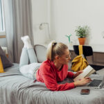 A college student sitting on the bed and taking notes from her laptop in her freshman dorm room.