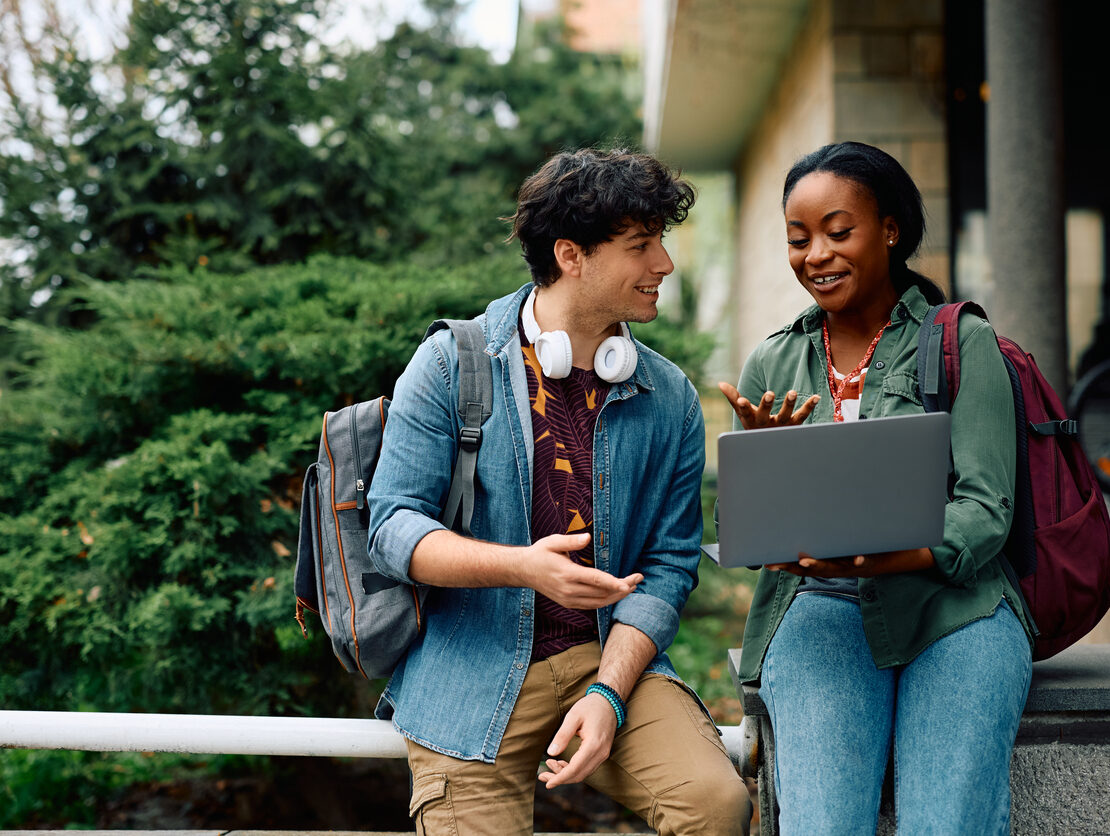 Two young college students smiling and laughing while looking at a laptop.