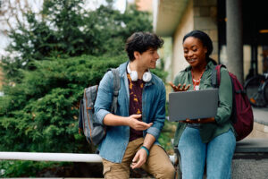 Two young college students smiling and laughing while looking at a laptop.