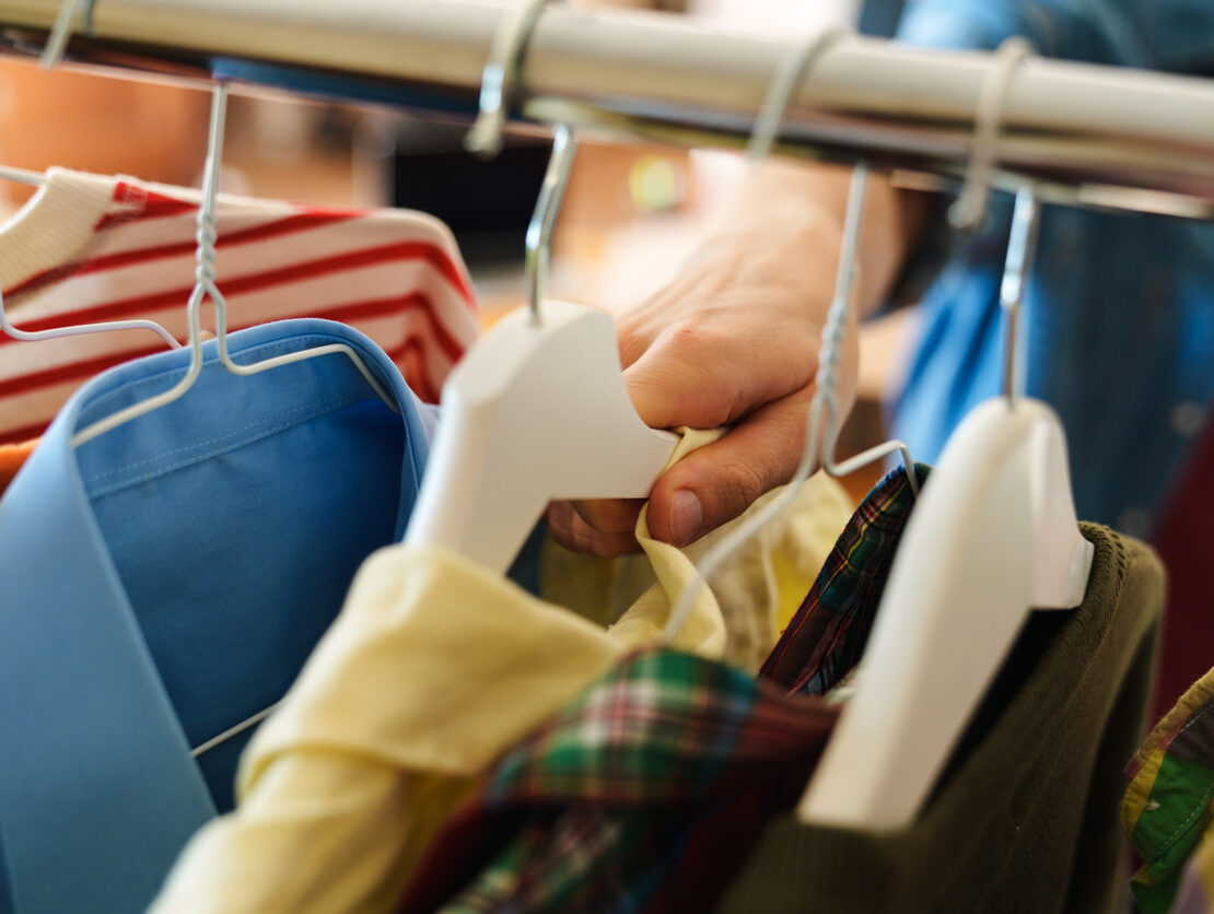 A man grabs a yellow shirt on a hanger in his closet