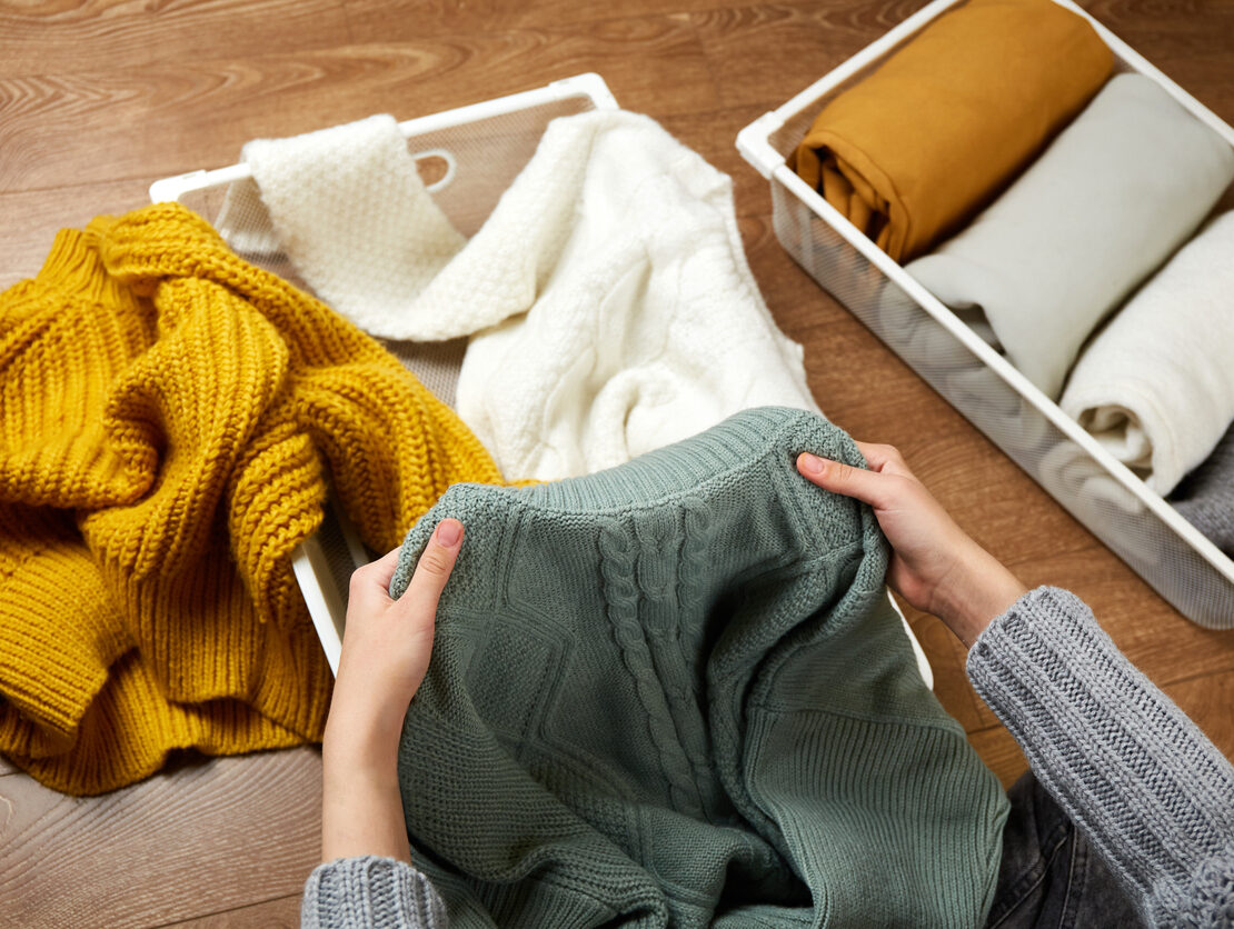 A young woman folding white, yellow, and green knit sweaters.