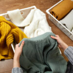 A young woman folding white, yellow, and green knit sweaters.