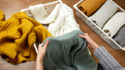 A young woman folding white, yellow, and green knit sweaters.