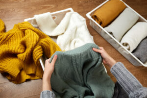 A young woman folding white, yellow, and green knit sweaters.