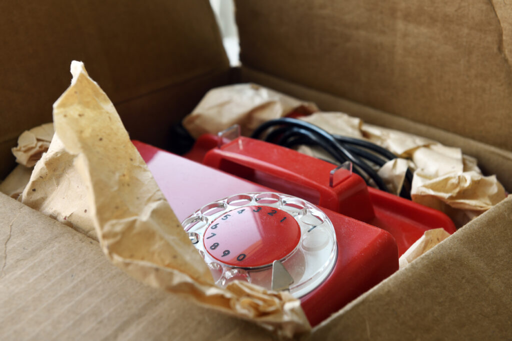 An old, red rotary phone packed away in a box for self storage.