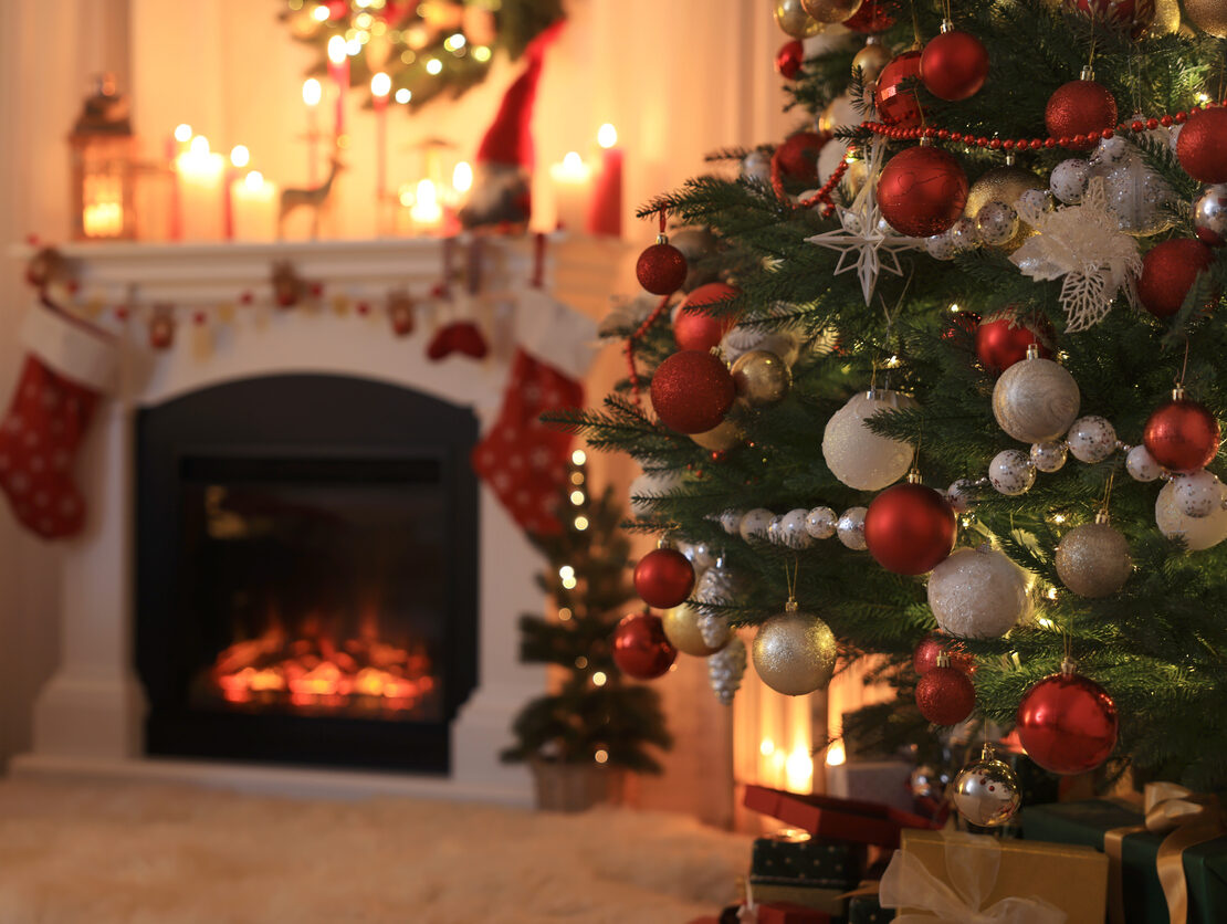 A living room decorated for Christmas with a Christmas tree and roaring fireplace.