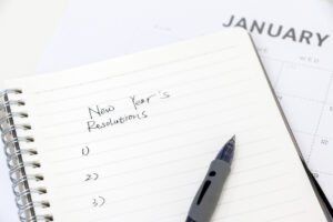 A pen rests on a notebook where someone has written “New Year’s Resolutions” and a blank list numbered one through three.