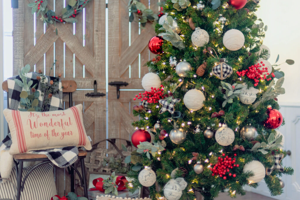 A Christmas tree decorated with plaid ornaments and rustic baubles next to a chair with a throw pillow and plaid blanket.