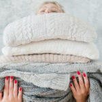A woman holding a thick stack of blankets and sheets.