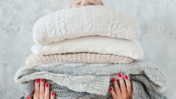 A woman holding a thick stack of blankets and sheets.