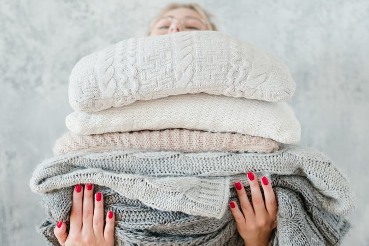 A woman holding a thick stack of blankets and sheets.