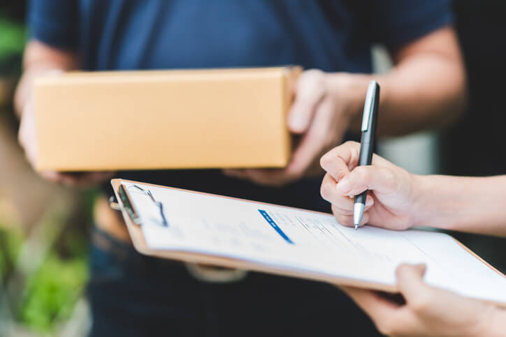 A woman signing on a clipboard to accept a delivery.