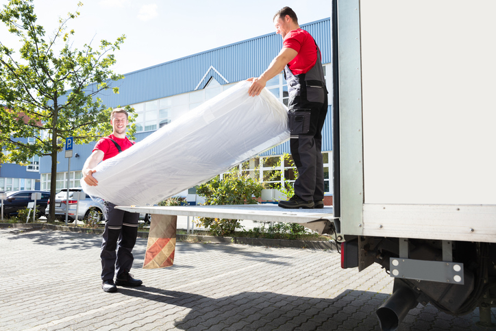 Two men carrying a mattress in a protective cover onto a moving truck.