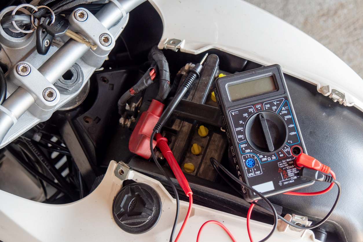 A motorcycle battery with a digital multimeter connected to test voltage.