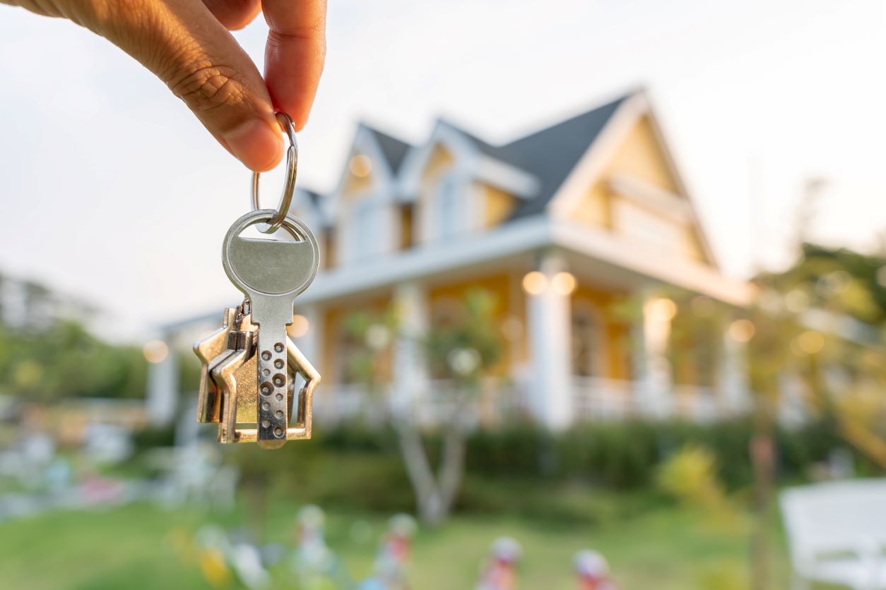 Someone holding keys with a house in the background